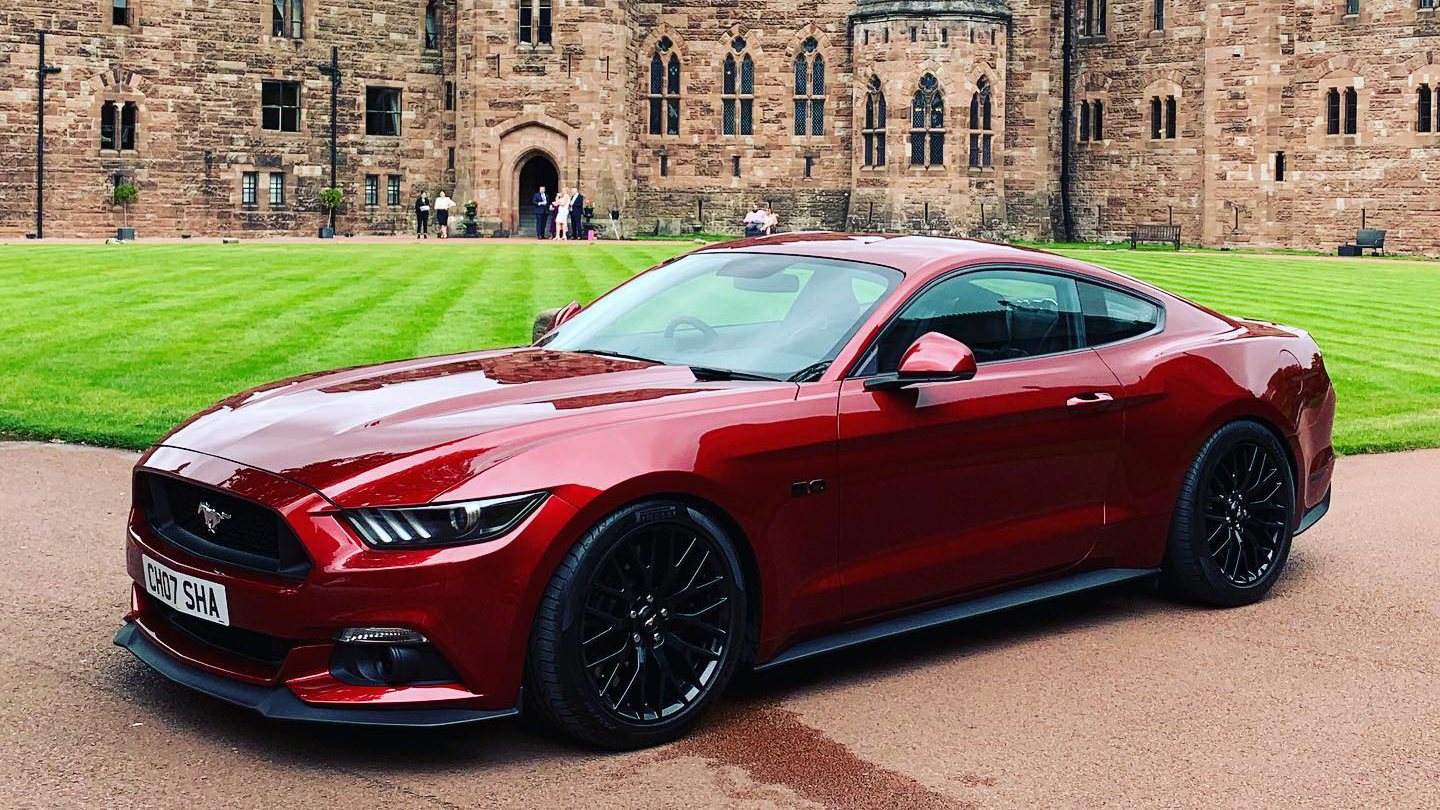 Left view of Cherry-red ford Mustang with a large wedding venue in the background