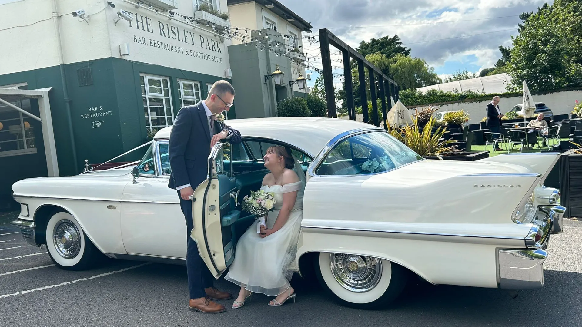 Bride and Groom with a classic White Cadillac. Bride seating on the rear seat and groom keeping the door open for her.