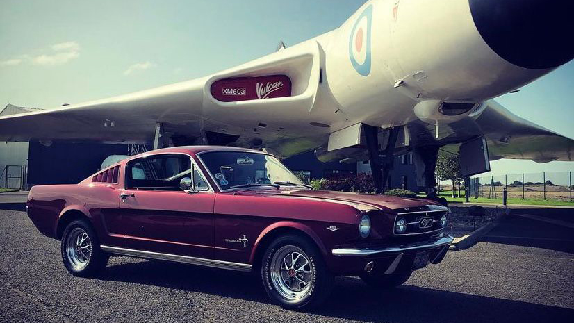 Classic Ford Mustang with chrome wheels parked underneath a classic Vulcan Plane