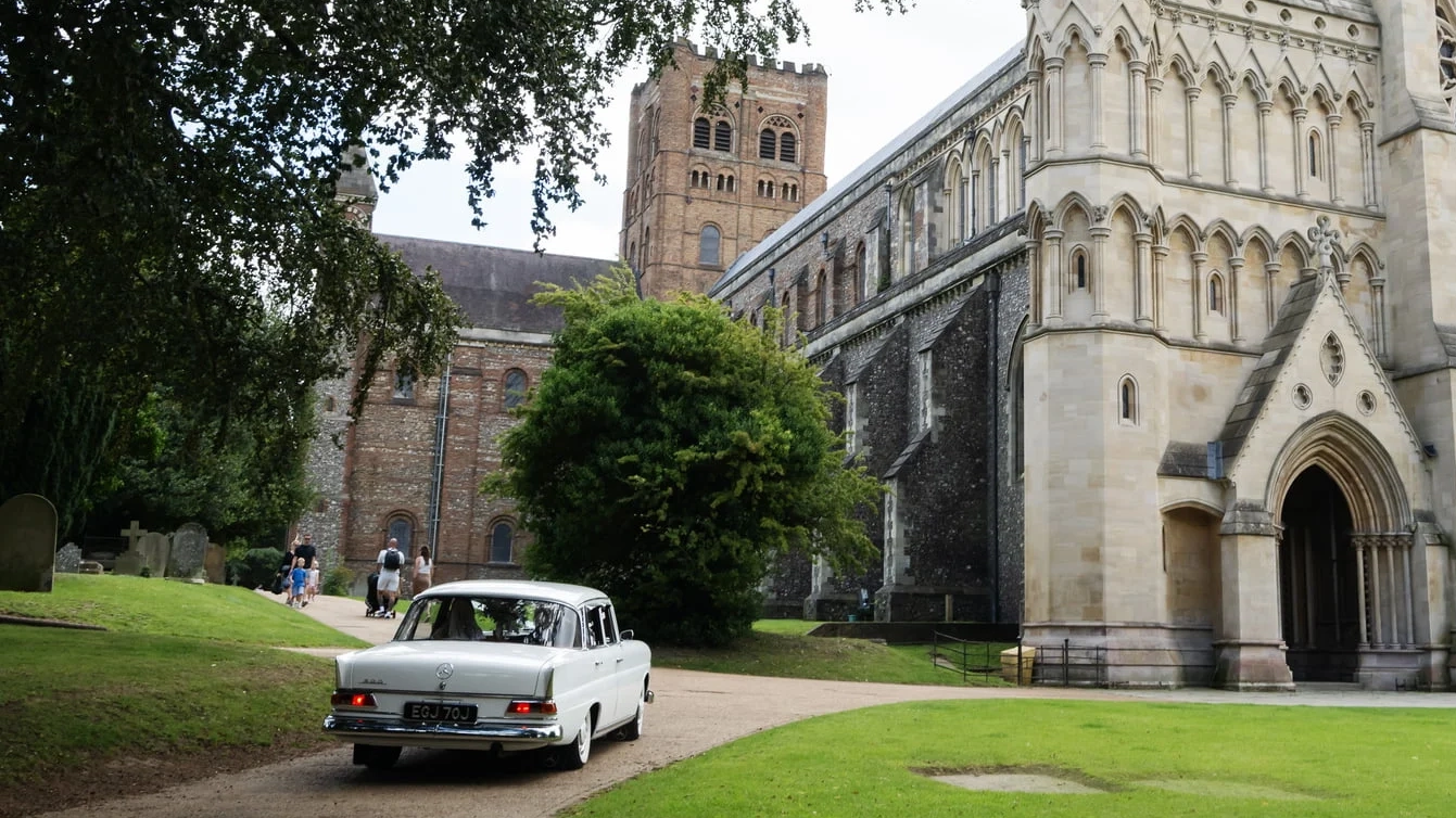 White Classic Mercedes Fintail driving towards ceremony, St Albans Cathedral in the background