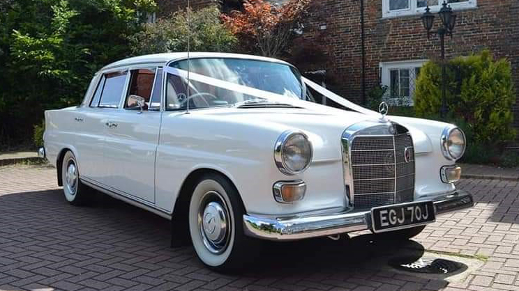 Front right side view of classic white Mercedes decorated with White ribbons, fat white wall tires and plain chrome wheel caps