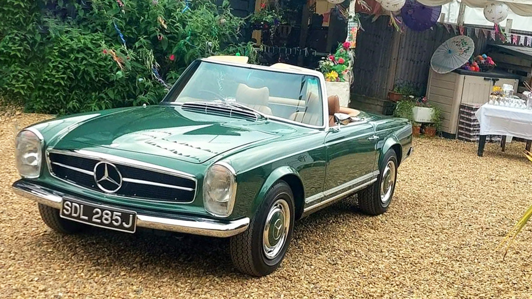 Convertible Aqua Green Classic Merces parked on a gravel path with entrance to weding marquee in the background