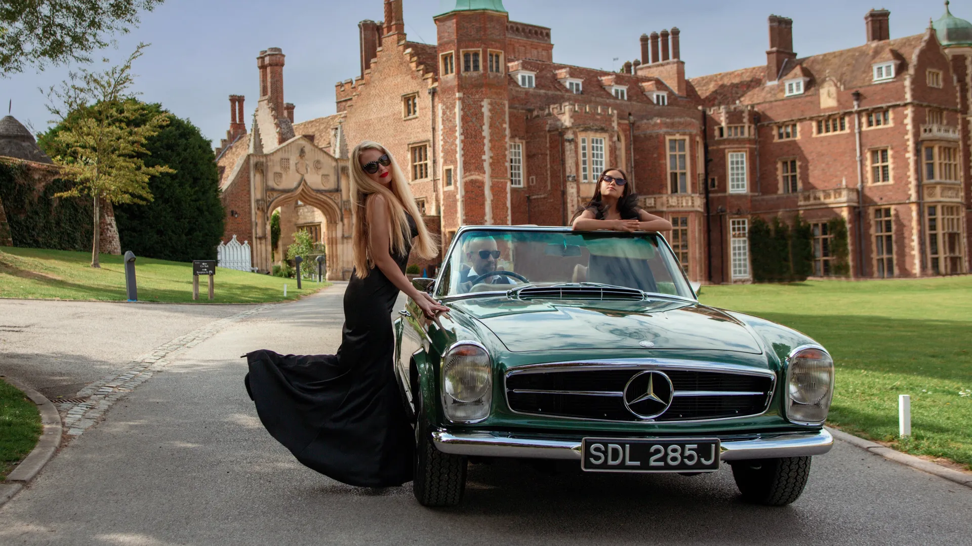 Front view of Classic Mercedes Convertible in Aqua Green with two bridesmaids wearing black dresses in front of a Castle-like wedding venue