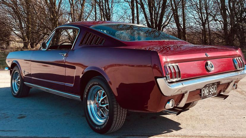 Left rear view of Classic Ford Mustang in Cherry Red with chrome bumper and chrome Alloy wheels in a winter backgroung with trees with no leaves.