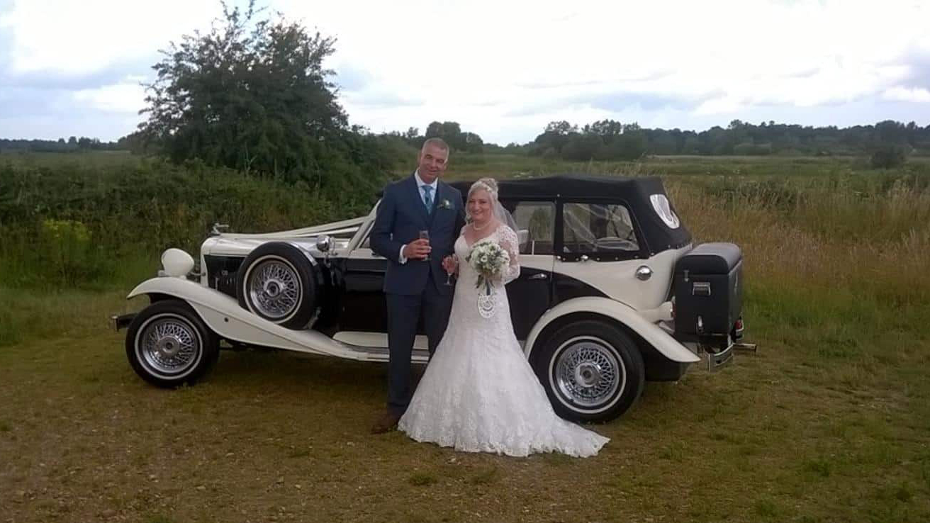 Bride and Groom standing in front of a Black & White Beauford with convertible black soft top roof closed.