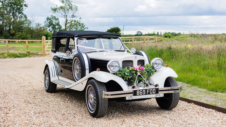 Black & White Beauford Convertible with black soft top roof closed, green foliage decorated on front chrome bumper and white ribbons.