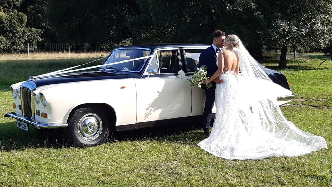 Bride and Groom standing by a classic Daimler Limousine in Ivory with Black Roof and Bonnet.