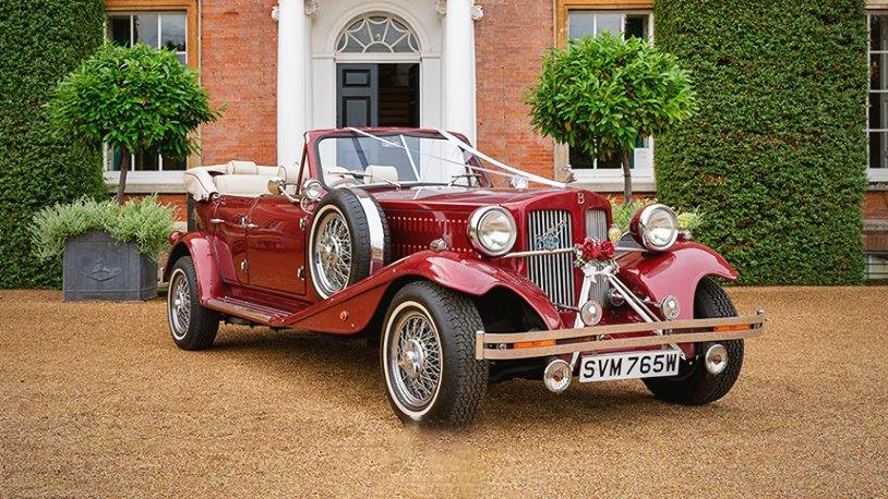 Front Right view of Burgundy Beauford with convertible soft top roof open, spare wheel mounted on the side of the vehicle and decorated with white ribbons