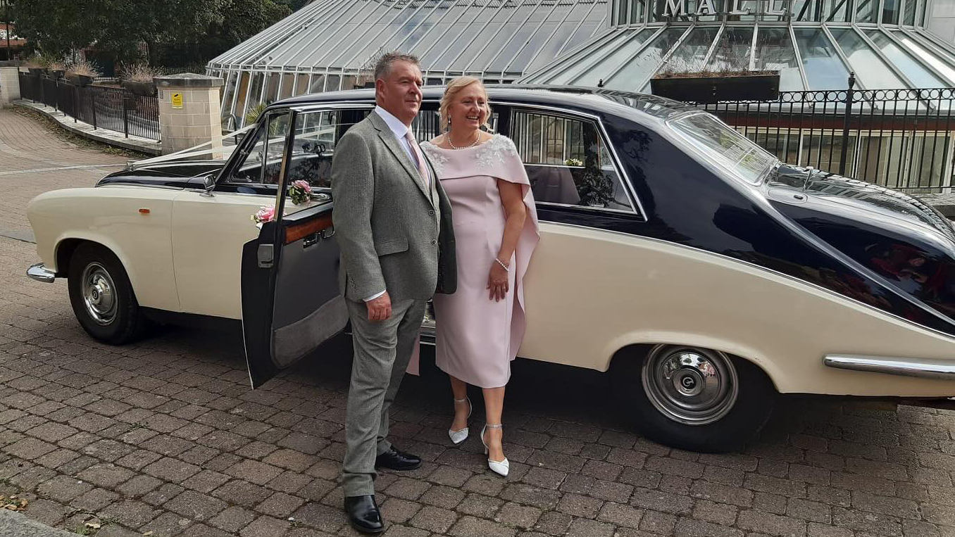 Black & Ivory Daimler DS420 with Bride wearing a light pink dress and groom with a silver suit.