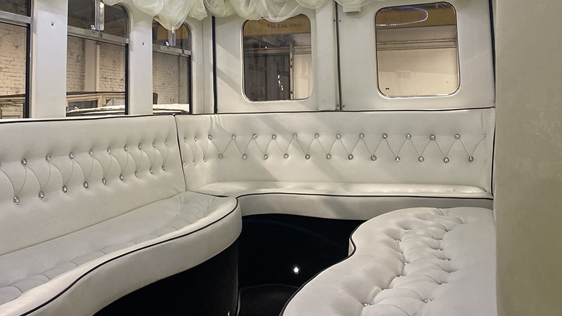 Cream leather interior inside vintage bus with bench seats all around, large windows on the side and back and black carpet.