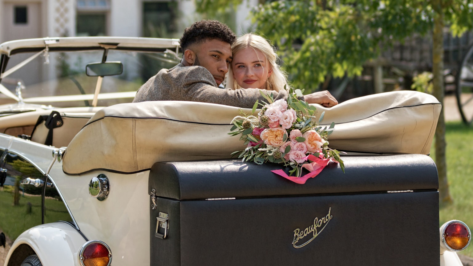 Bride and Groom seating in the rear seats of a convertible Beauford with roof down. Both are looking back for photos