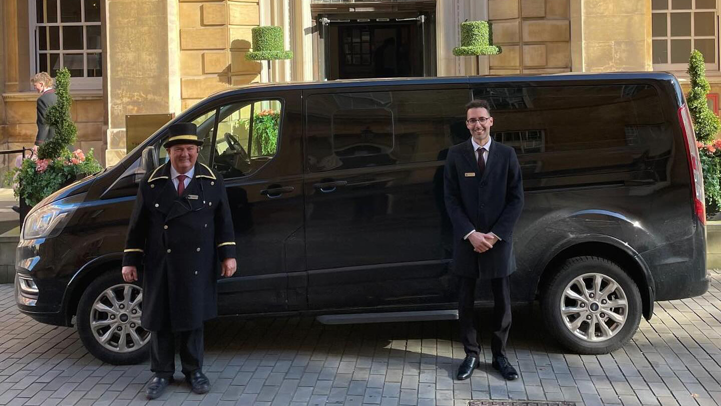 Black Ford Mini Bus in front of hotel with Hotel Doorman and Toastmaster