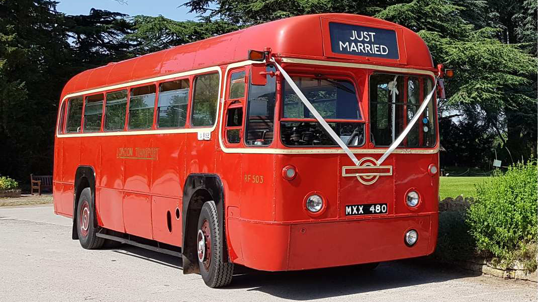 Front right view of classic single decker red bus decorated with white wedding ribbons