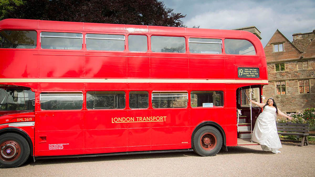 Bride wearing a white dress standing on the rear open platform of a Red Routemaster bus