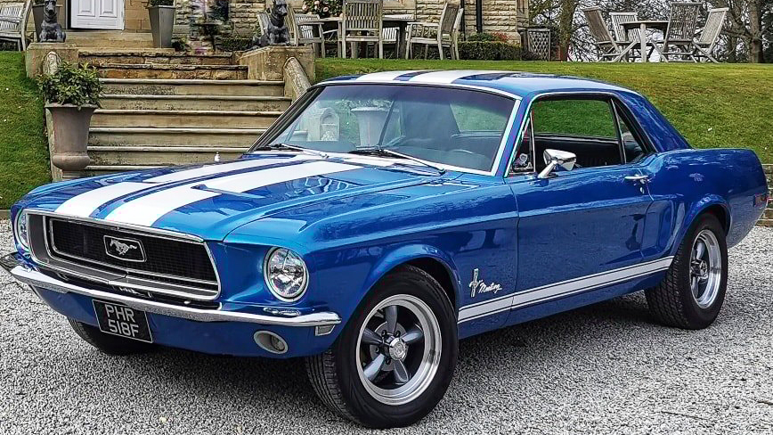 Classic Blue Ford Mustang with two white stripes across bonnet and roof in front of a wedding venue