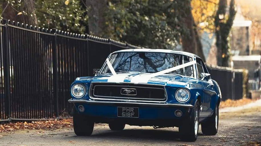 Classic Blue Ford Mustang driving in the street of Bradford with White Ribbons