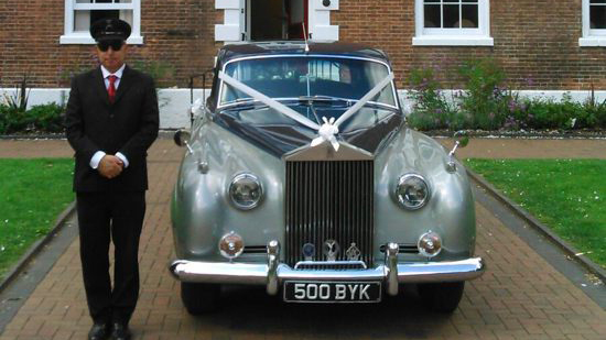 Classic Black & Silver Rolls-Royce silver Cloud dressed with white ribbons and bows with fully uniformed chauffeur standing by the vehicle