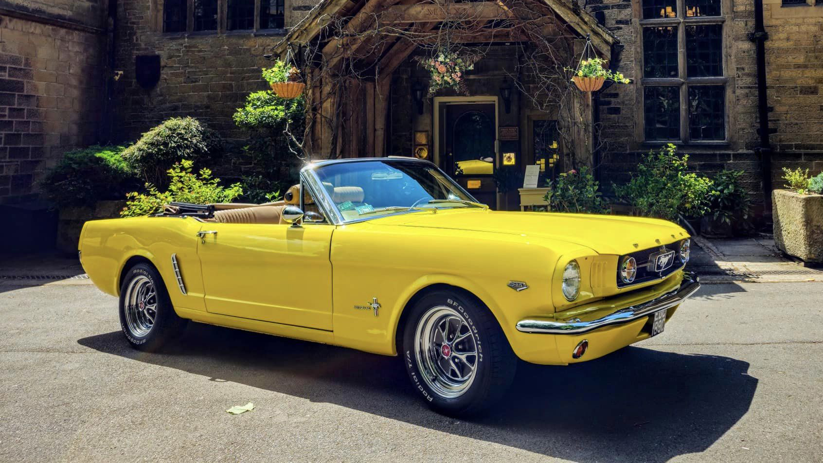 Classic Ford Mustang in Yellow with convertible roof open in front of a wedding venue