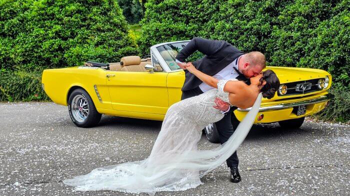 Groom kissing his Bride in front of a yellow convertible Ford Mustang