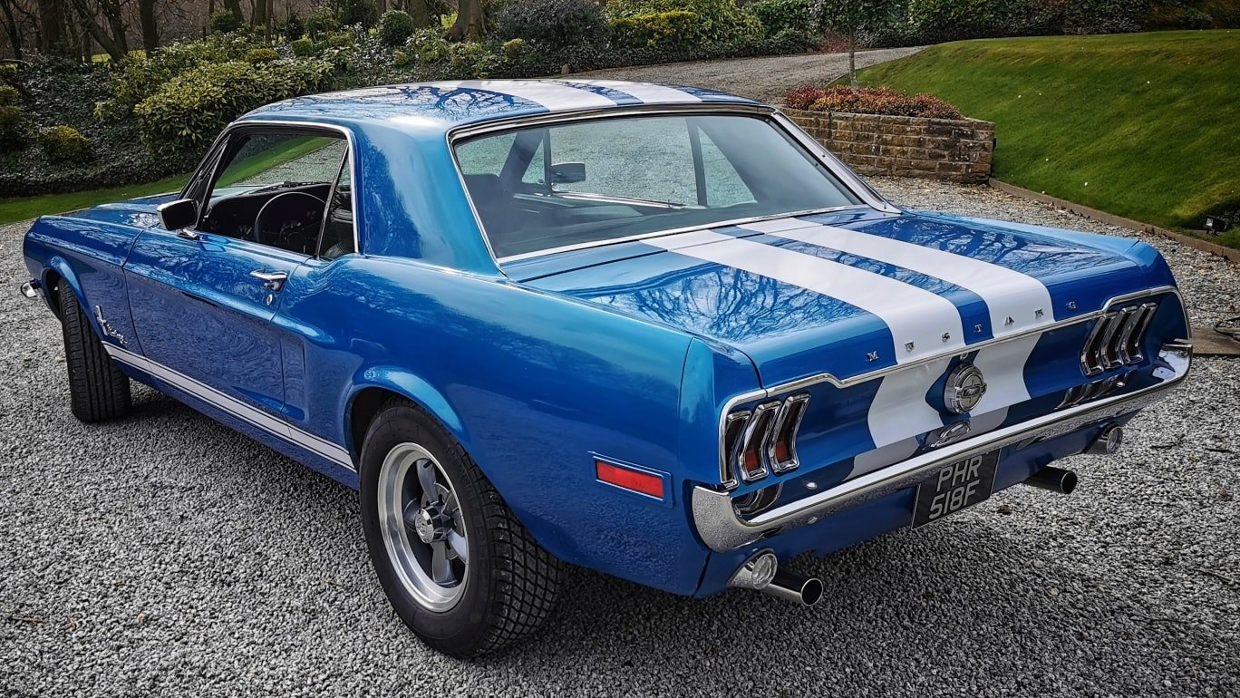 Rear view of Classic Blue Ford Mustang with two white stripes across roof and boot.