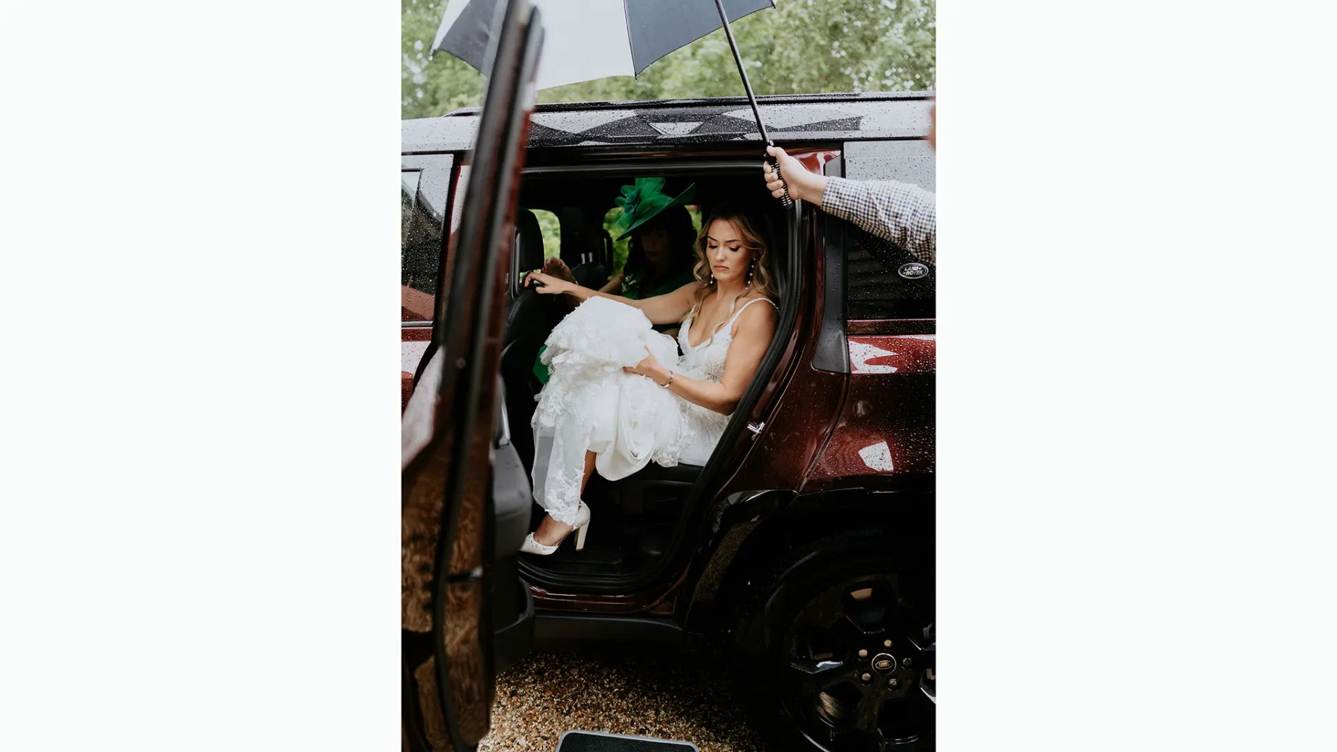 Bride wearing a white dress seating in the rear of a Landrover Defender with door open