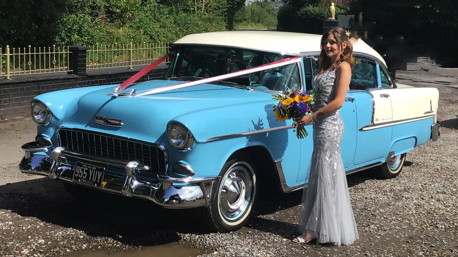 Bride standing by a classic Blue and White Chevrolet decorated with Red Ribbons