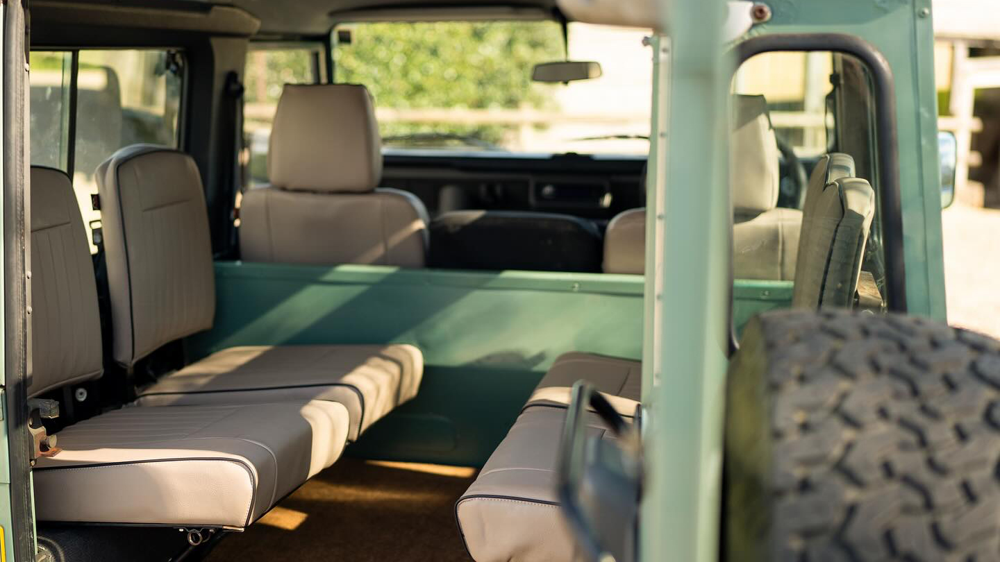 Rear door at the back of a Green Land Rover Defender open showing 4 cream leather seats facing each others