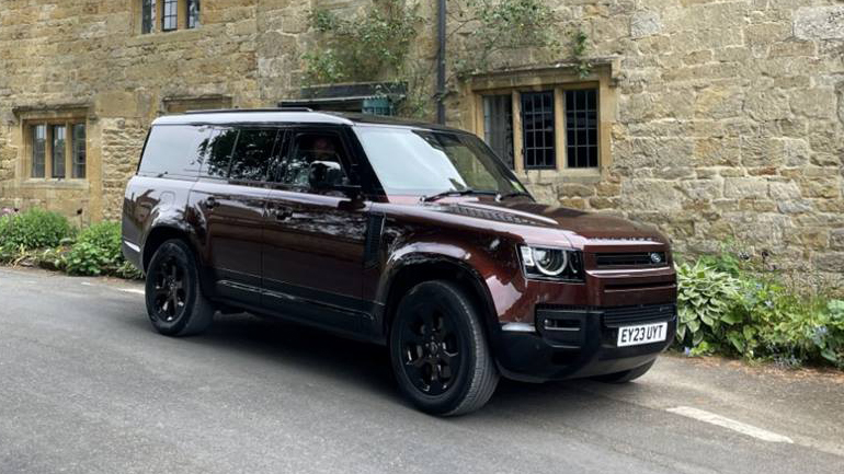 Modern Land Rover Defender 130 in Sedona Red decorated with white ribbons parked in the street of a small cotswolds village