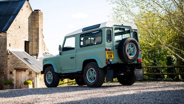 rear view of green classic Land Rover Defender with spare wheel attached to the back of the vehicle