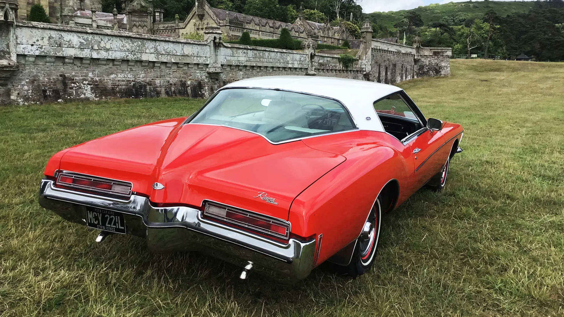 Rear view of classic american Buick from the 70s with red boot and white roof and large rear chrome bumper.