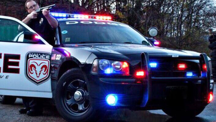 American Dodge Charger pursuit police car with police lights on and police officer standing by the vehicle