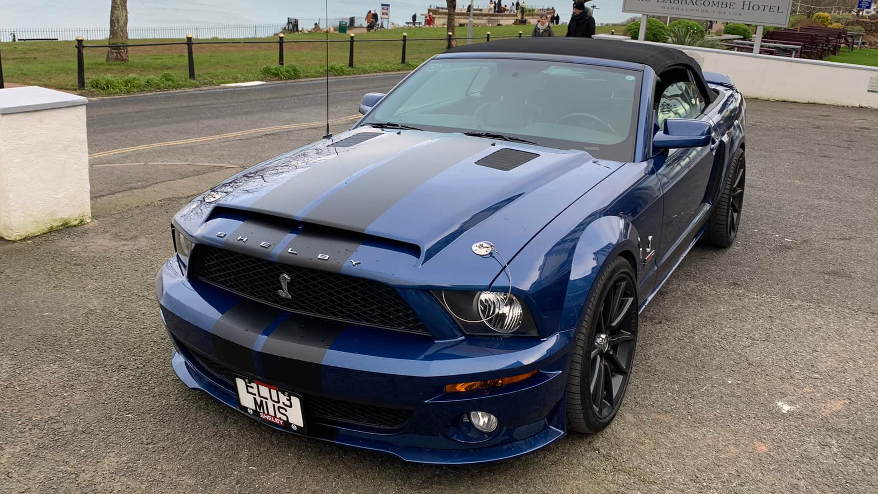 Front view of dark blue Ford Mustang with black stripes on front bonnet