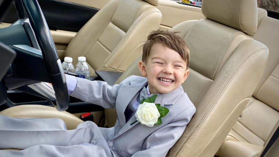 A very happy page boy seating in the driver's seat inside Ford Mustang Convertible with cream leather interior