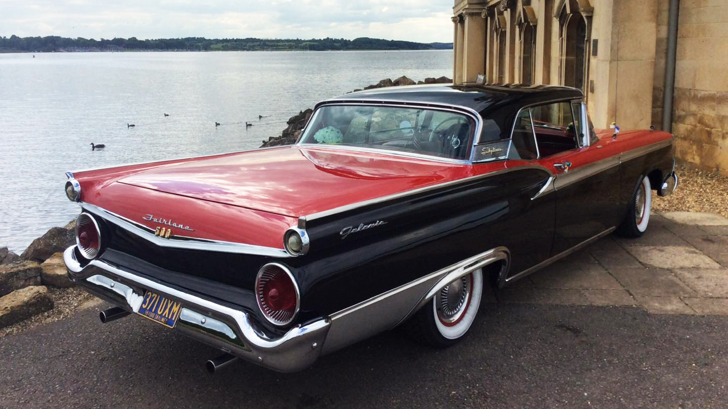 Rear view of classic american Ford Fairlane with black roof up and large chrome rear bumper.