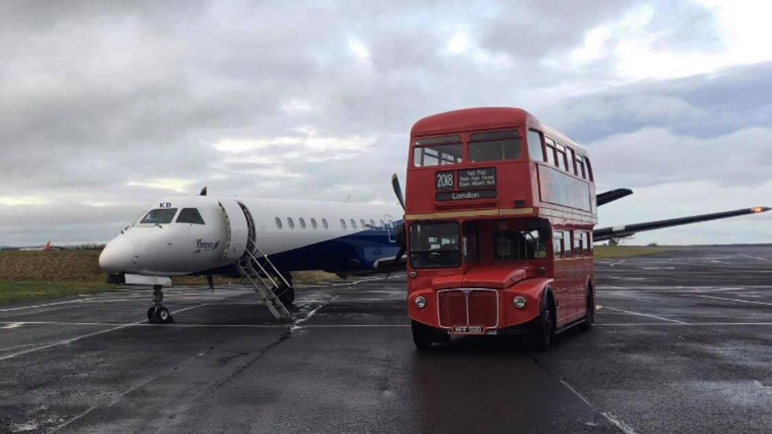 Double Decker Vintage Red Bus parked on an air field by a plane