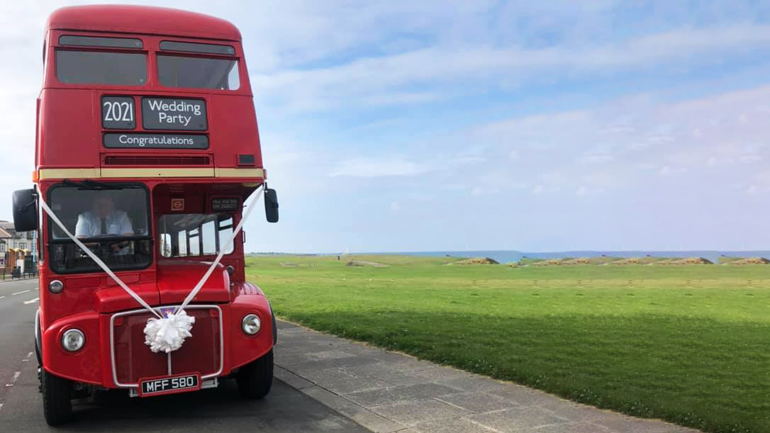 Front view of red Double Decker Routemaster bus parked by the sea side in Tyne and Wear dressed with white wedding ribbons and bow