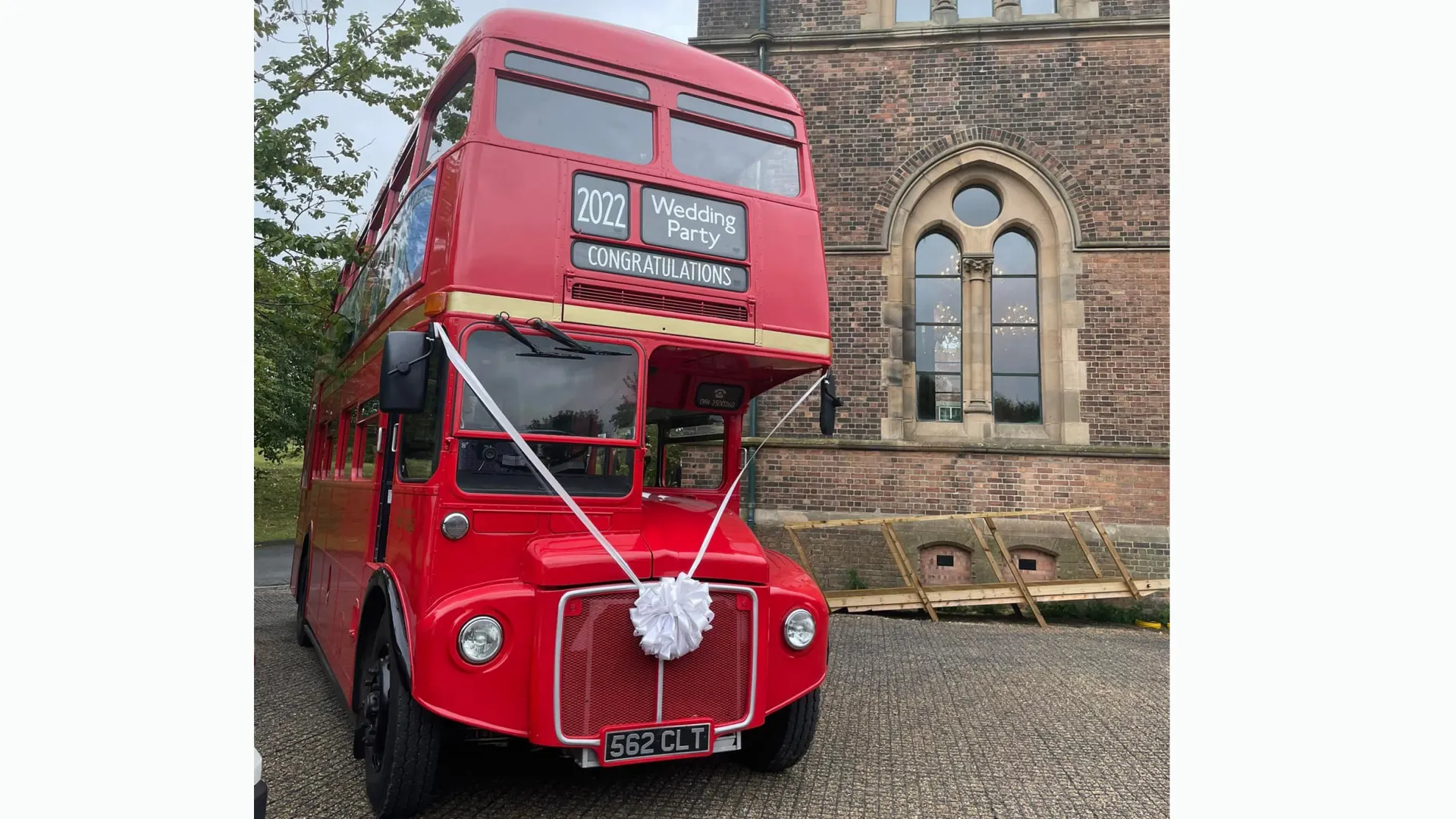 Classic Red Double Decker Bus with white ribbons parked in front of a wedidng church