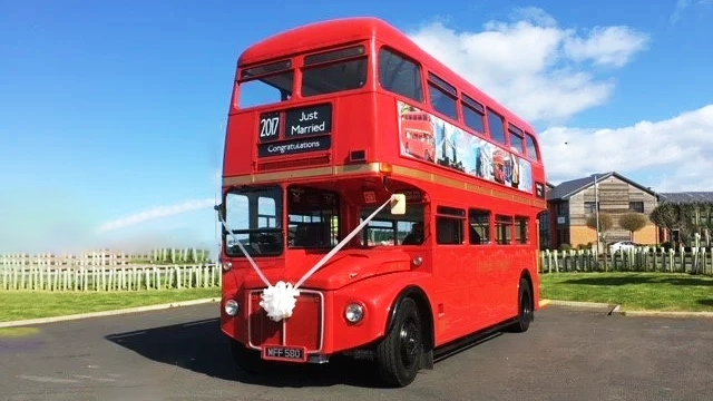 Double Decker Red Routemaster bus decorated with white wedding ribbons and bows