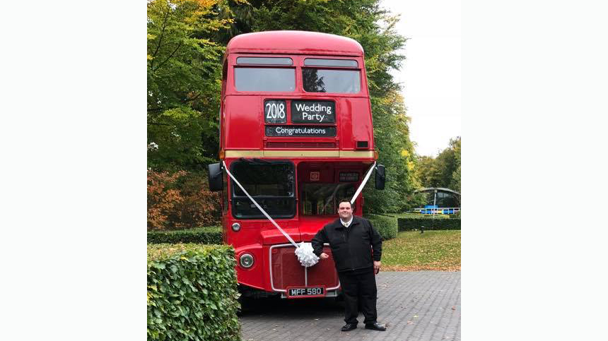 Bus Conductor standing in front of a red Routemaster Bus decorated with white ribbons