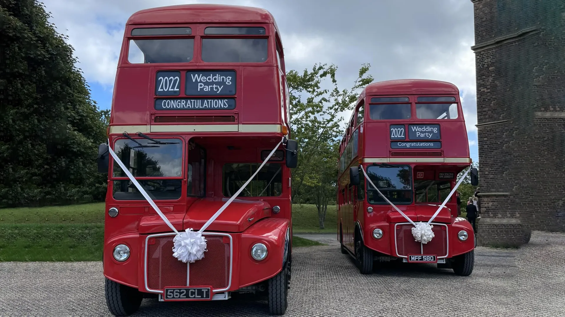 Two identical vintage routemaster buses parked in front of a church in Northumberland