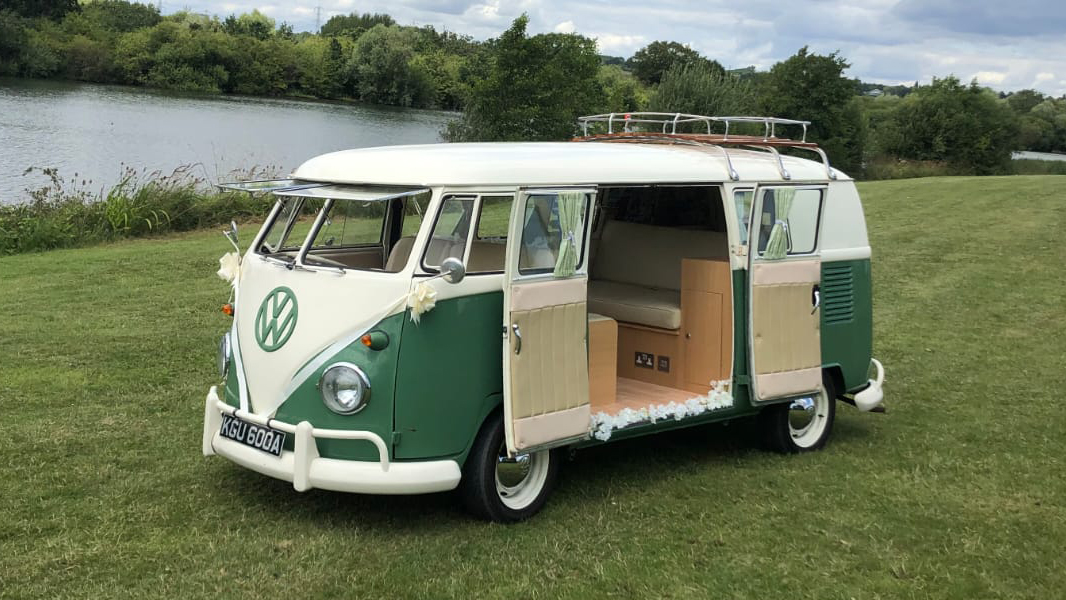 Classic Campervan with rear passenger door fully open parked in a green park with a lac in the background