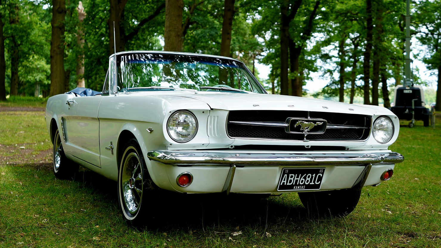 Right front view of classic american ford mustang with convertible roof down parked in a green forest