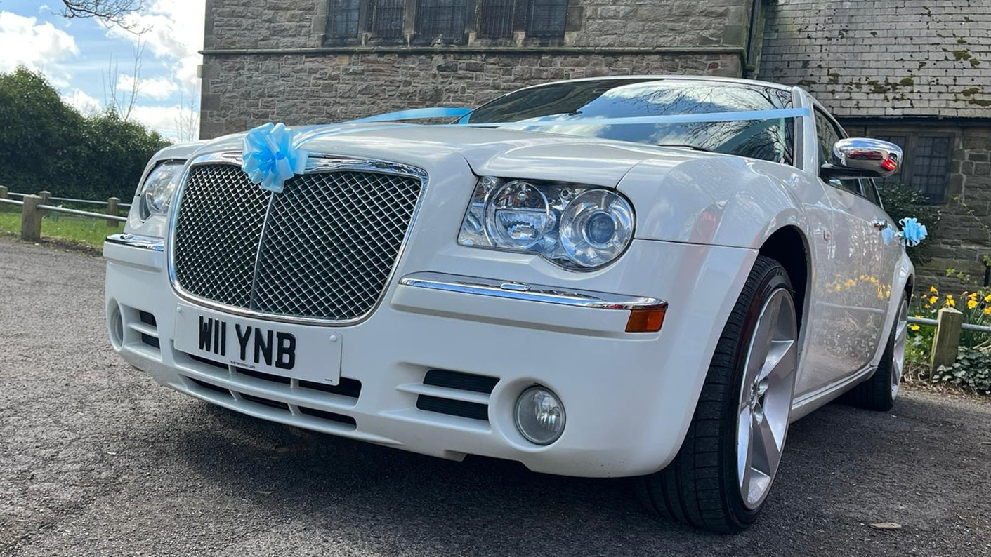 White Chrysler 300c Saloon Car parked in front of a church and decorated with turquoise blue ribbons and bows