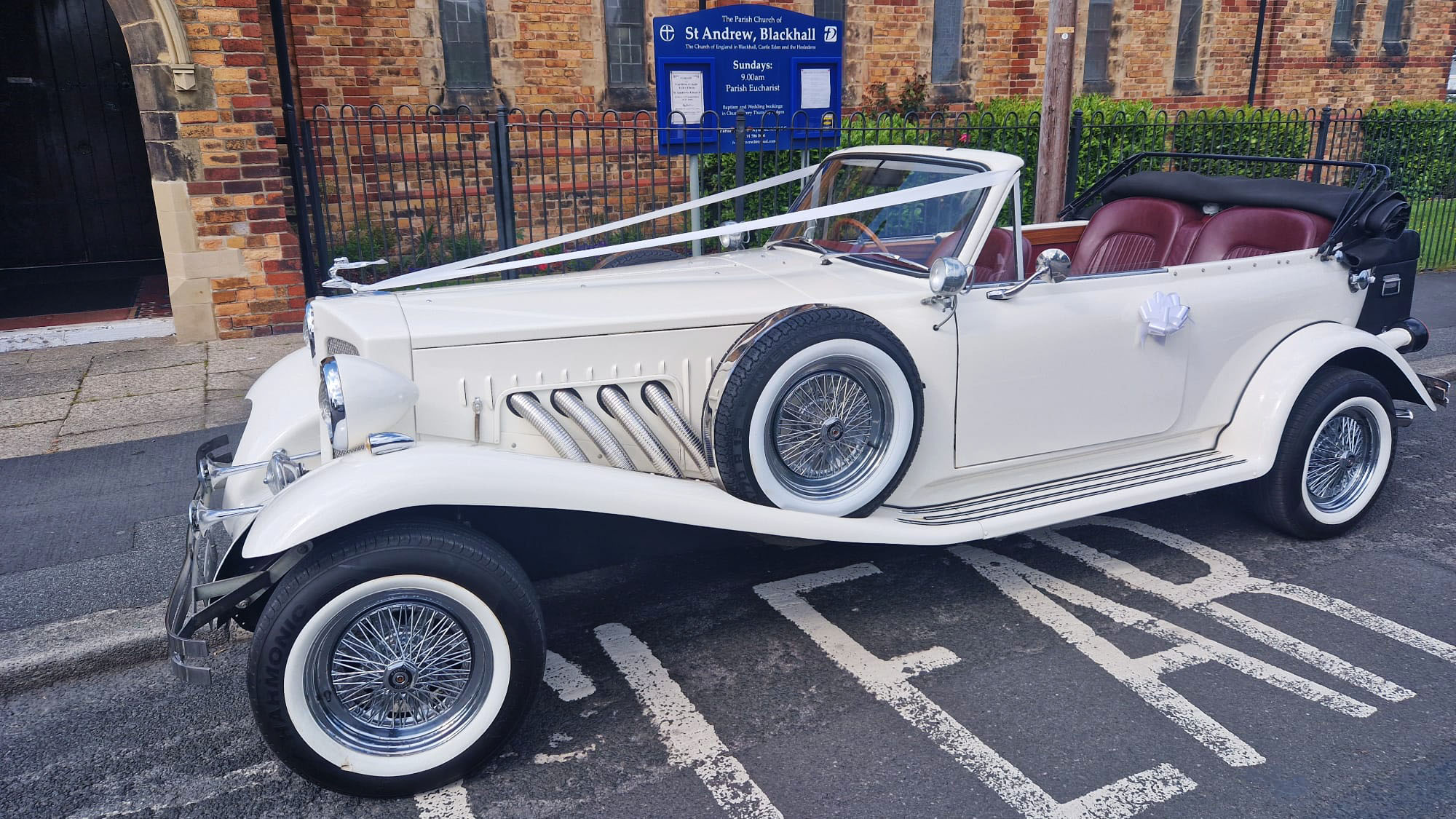 Left side view of a Beauford convertivle with roof open decorated with wedding ribbons and spare wheel mounted on the side of the vehicle