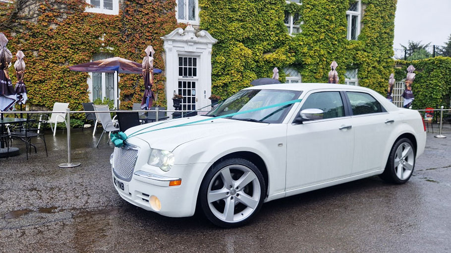 White Chrysler 300c Saloon Car with Green ribbons in front of a wedding venue in Durham