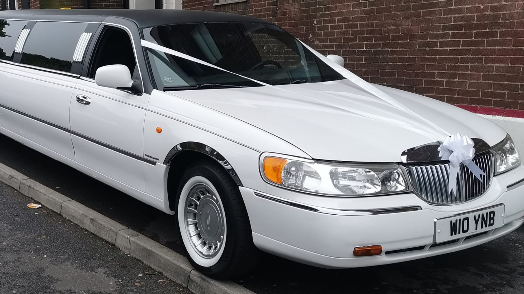 Front view of Stretched limousine with white wall tires, chrome grill and decorated with white ribbons and bows