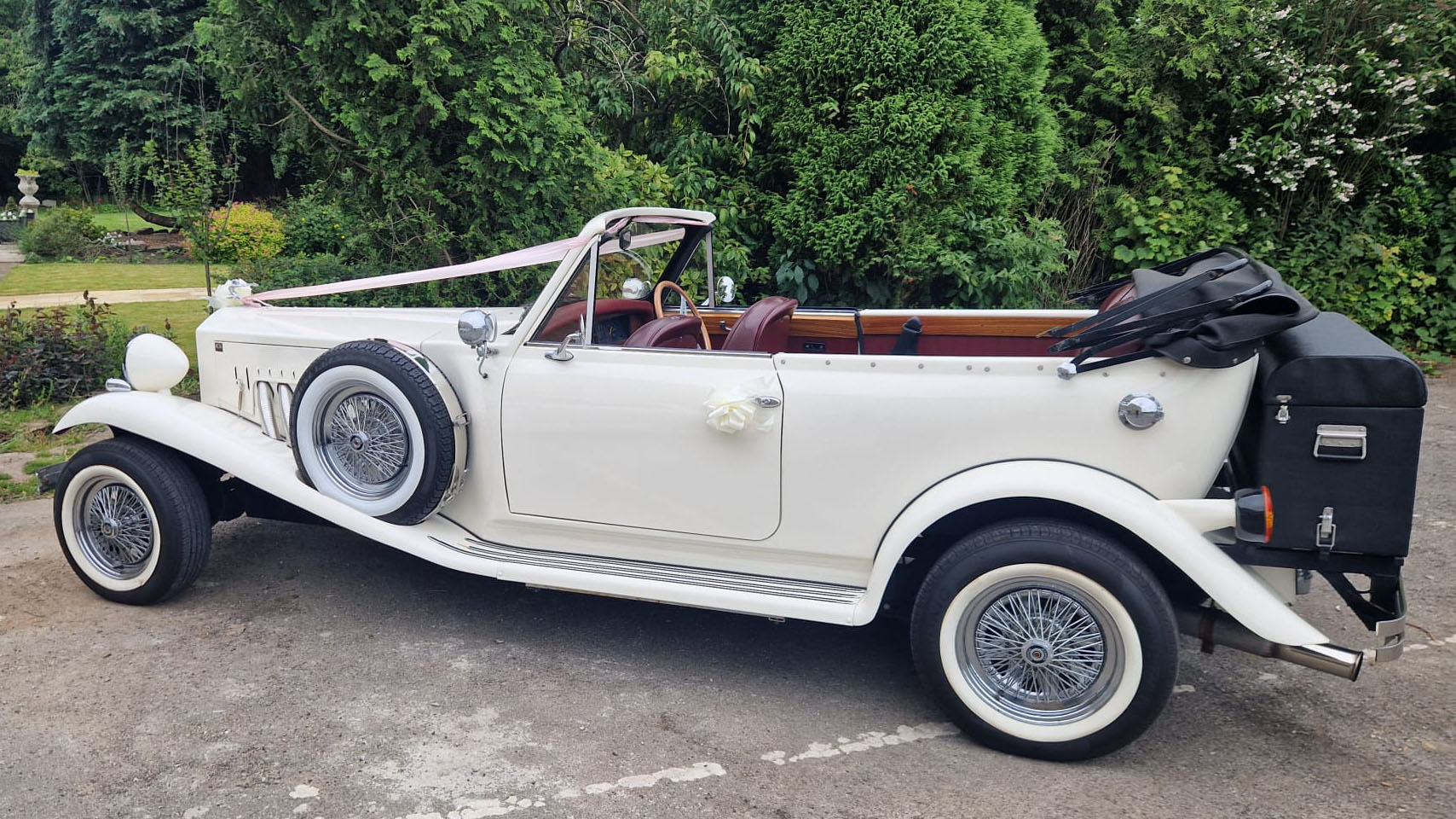 Left side view of a vintage Beauford with soft top roof open showing a Maroon leather interior and rear picnic trunk in black