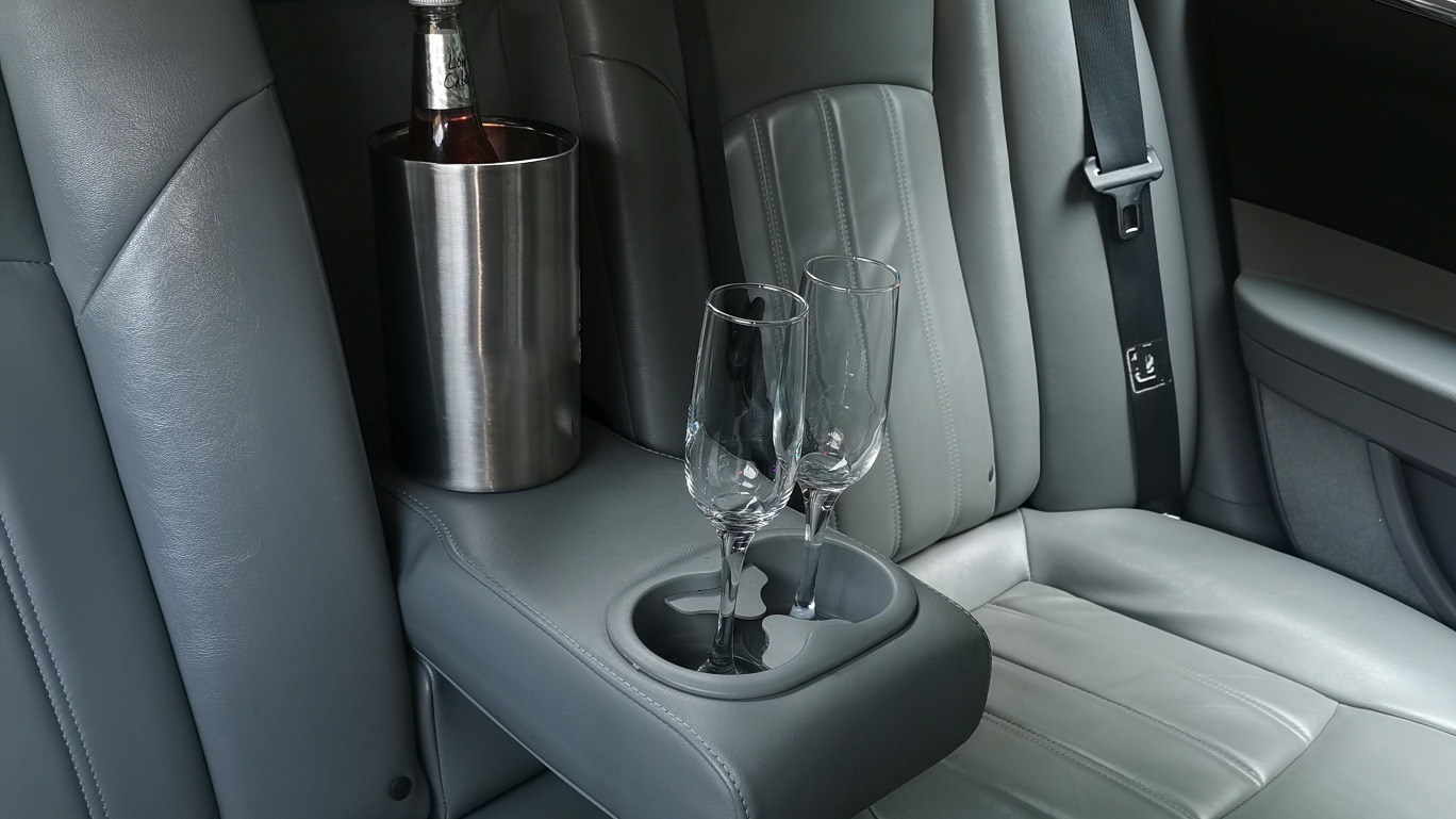 Greay leather interior inside a Chrysley 300c car with twoi empty champagne glasses and ice bucket with a bottle inside