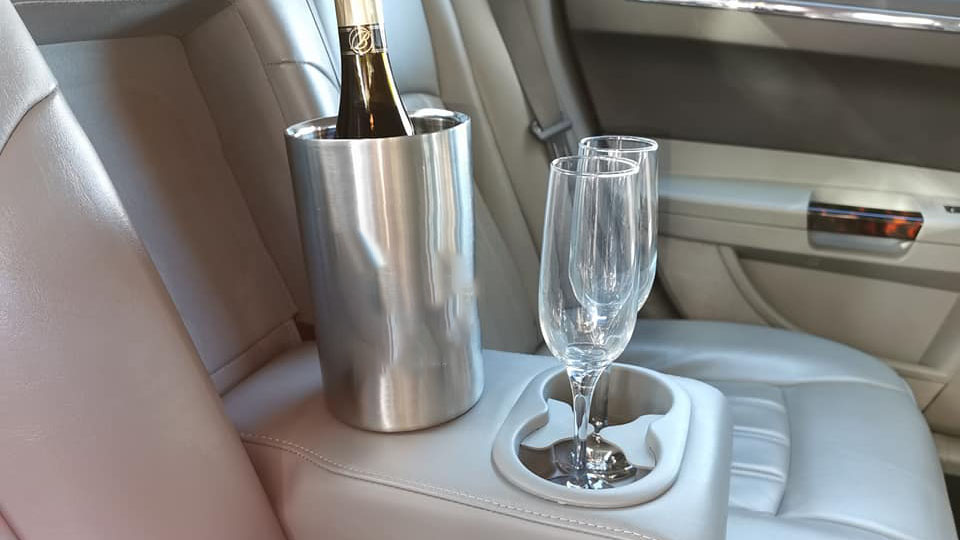 Two empty glasses of champagne and an ice bucket with a biottle of champagne on the rear seat of a Chrysler car