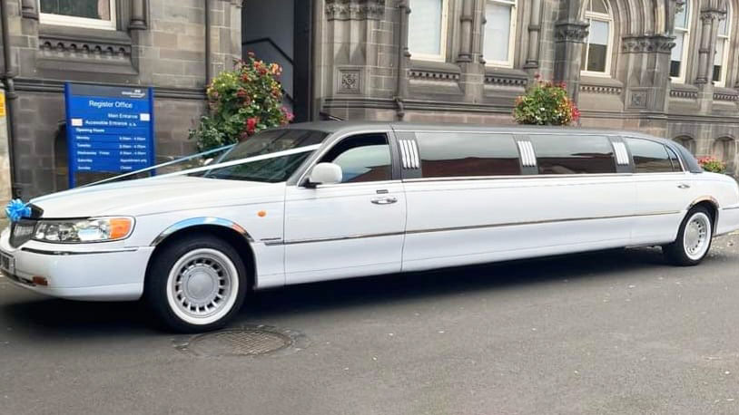 Left side view of a white Stretched limo with black roof